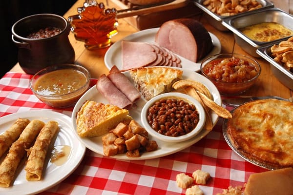 Traditional sugar shack feast with tourtière, baked beans, ham, and maple syrup on a checkered table